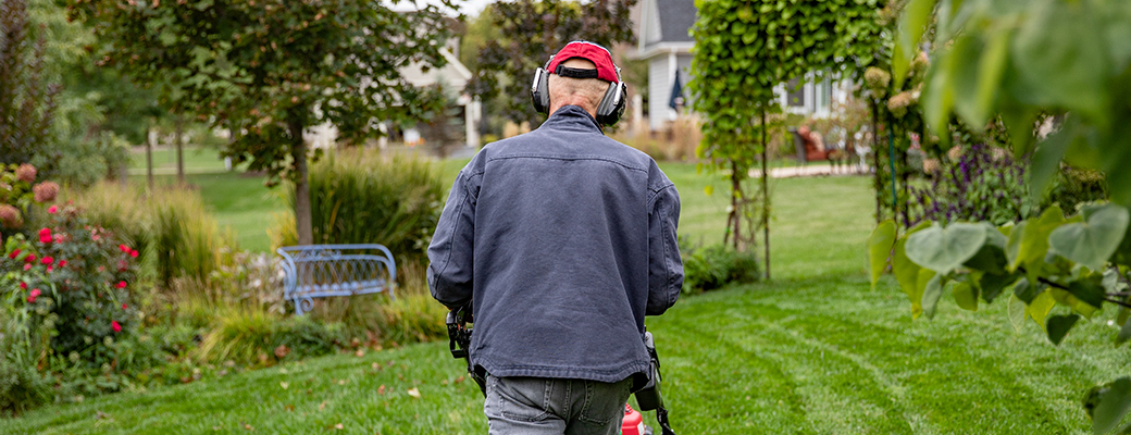 Image of senior male wearing protective earmuffs while mowing the lawn